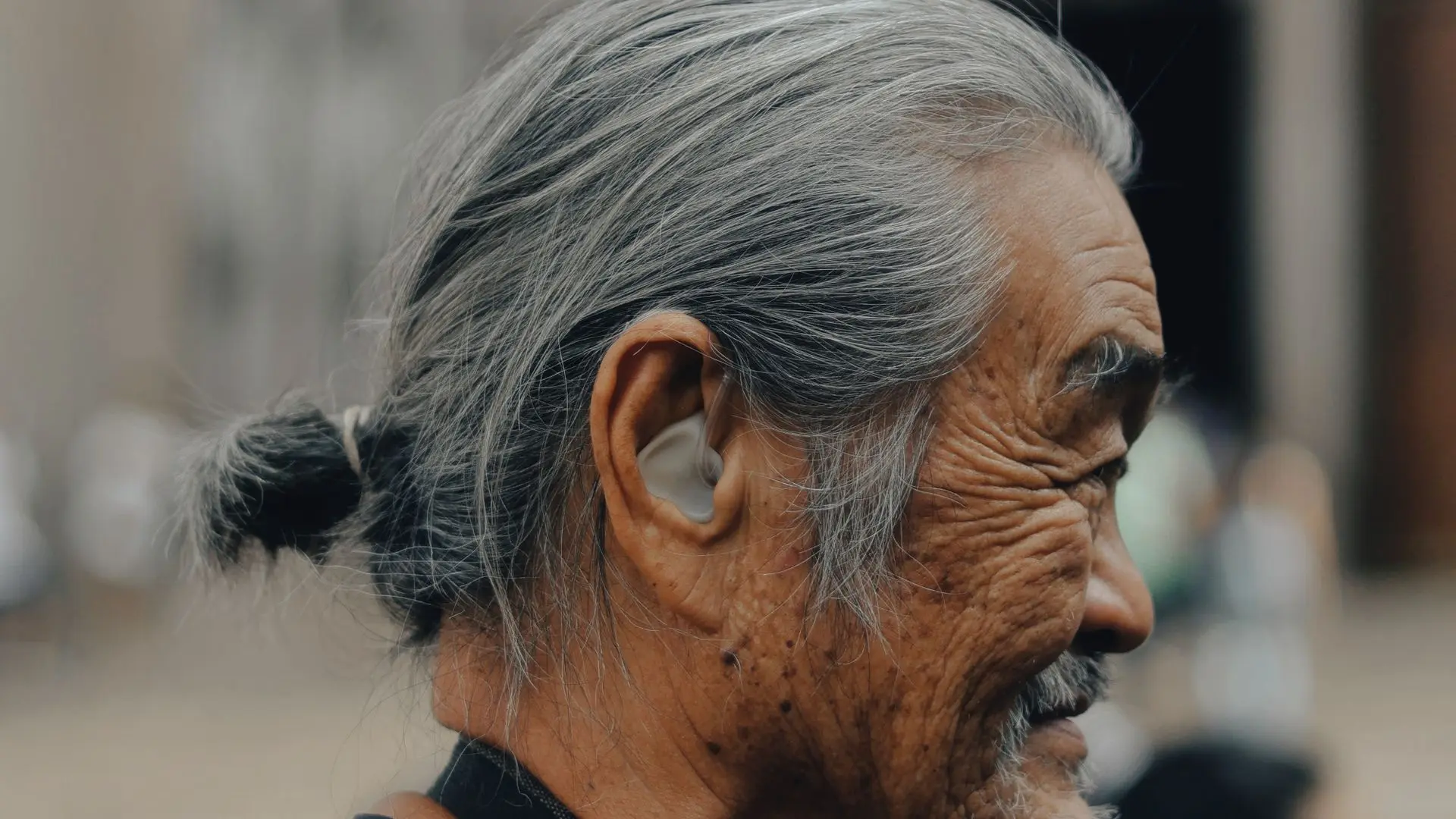 Hombre mayor sonriendo al aire libre con un audífono detrás de la oreja