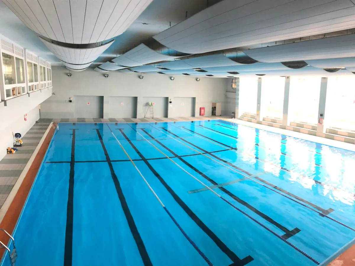 Piscina con cubierta telescópica de policarbonato abierta a medias, con el jardín al fondo