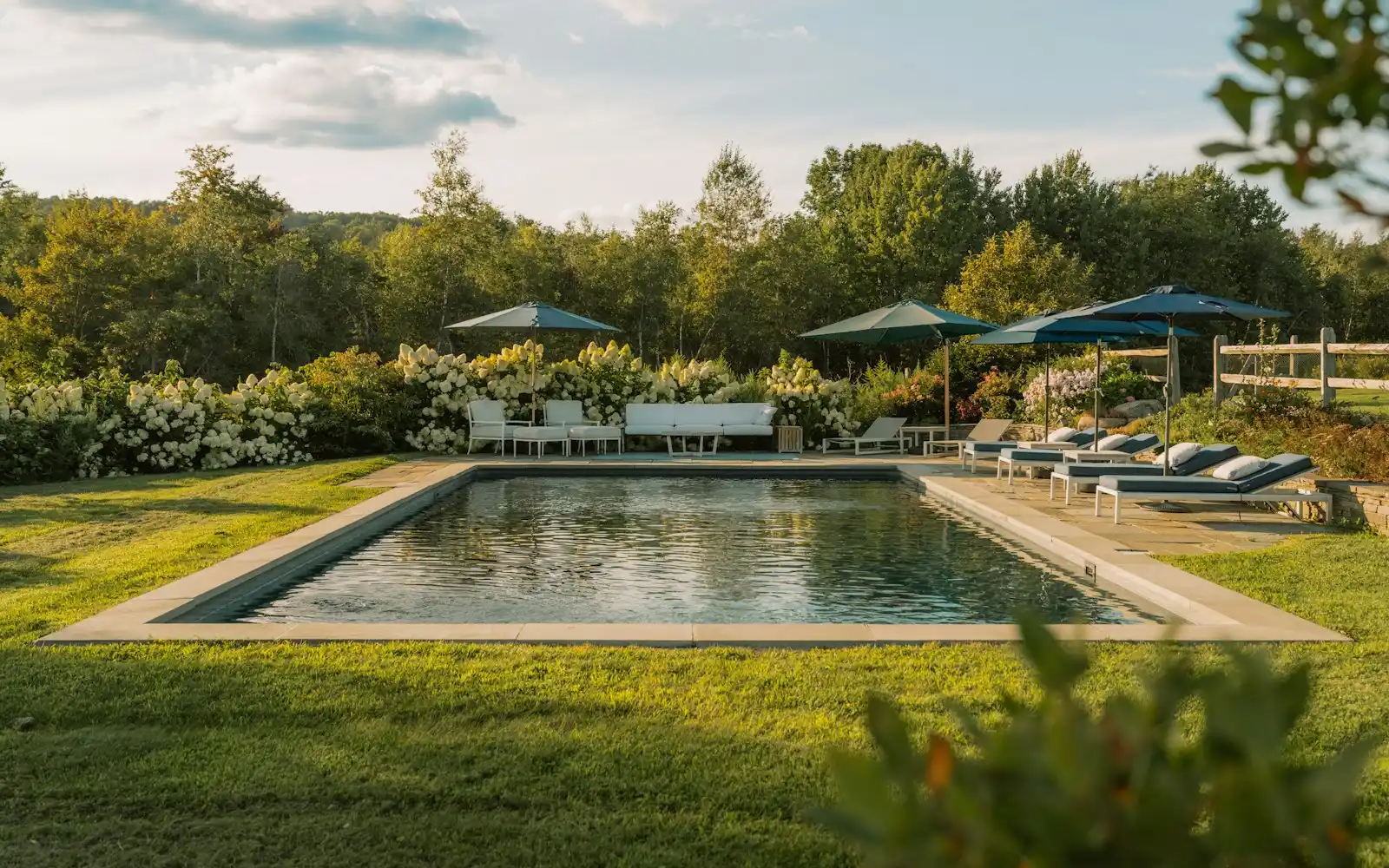 Piscina de obra rectangular con playa de piedra clara y jardín, en una casa de campo de la huerta de Murcia