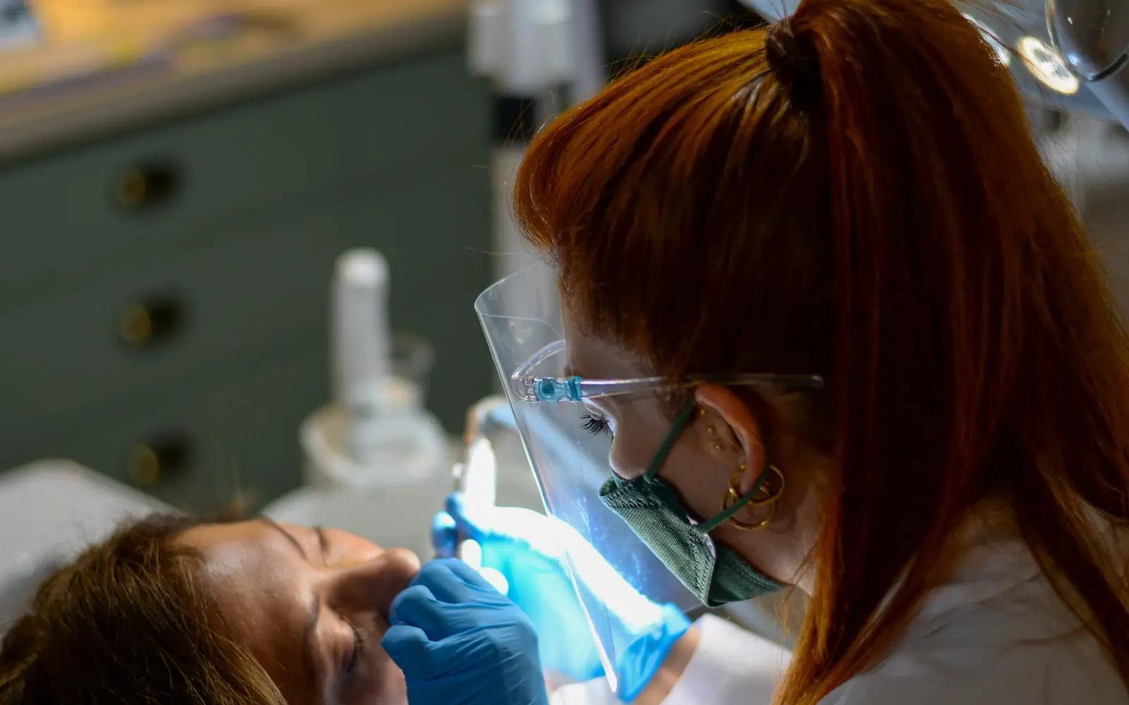Dentista atendiendo a una paciente en el sillón con la lámpara encendida