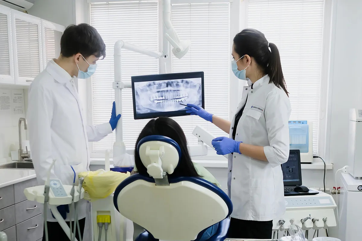 Dos dentistas revisan una radiografía en la pantalla del gabinete junto al sillón
