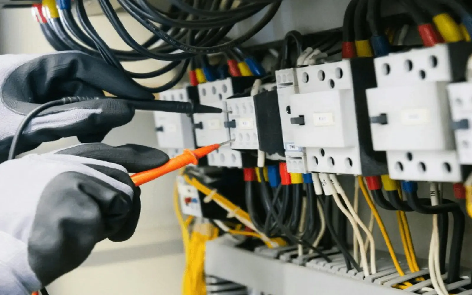 Electricista con equipo de protección midiendo con un comprobador en un cuadro eléctrico de vivienda recién montado