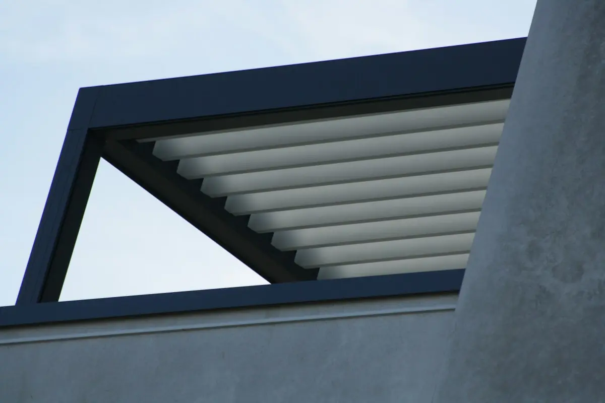 Pérgola bioclimática de aluminio antracita con las lamas abiertas en un jardín
